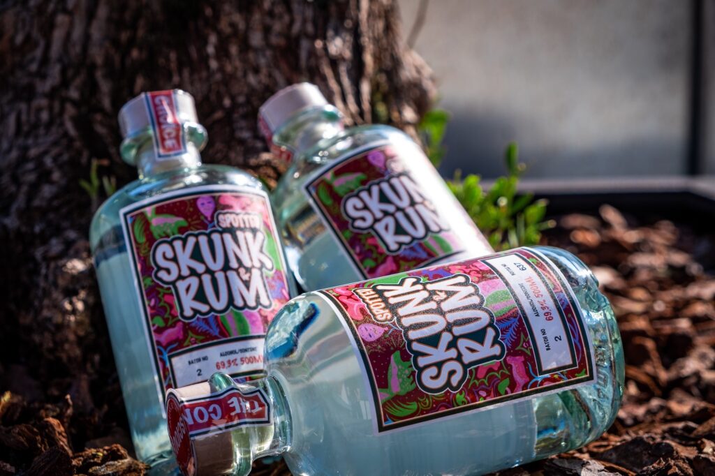 Drei Flaschen Skunk Rum Organic am Fuss eines Baumes im Sonnenlicht