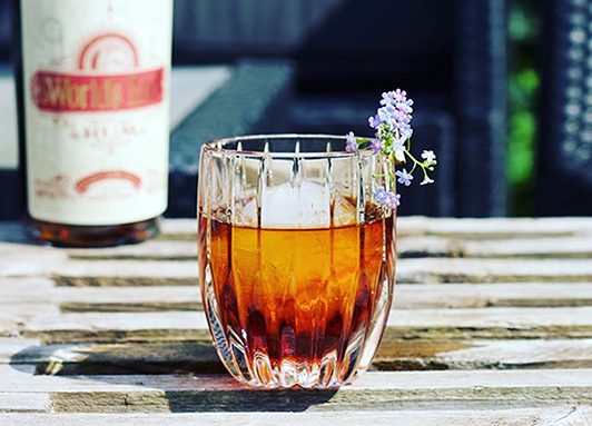 Gerührter Rum-Cocktail mit Eiskugel und Blume